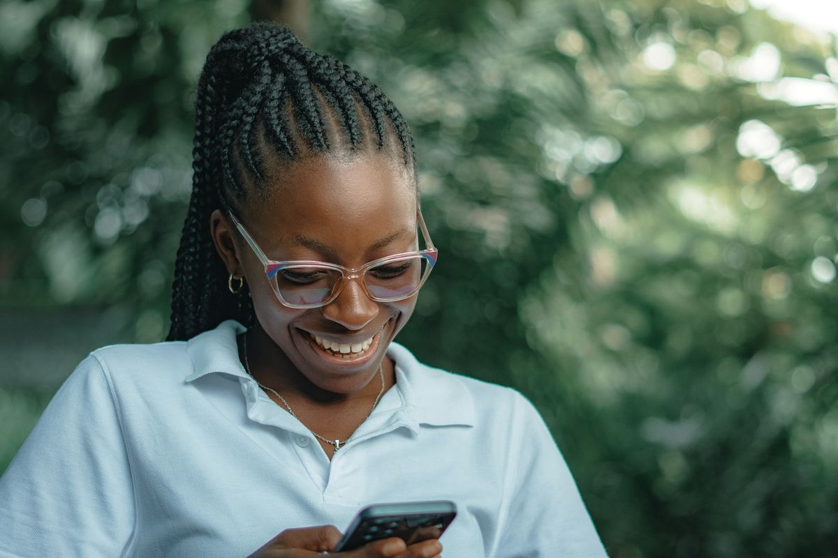 A smiling woman in glasses reads a message on her phone